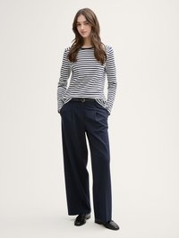 Gestreepte langekleding top in marineblauw en wit, gecombineerd met wijde marineblauwe broek en zwarte loafers. Minimalistisch design met een ontspannen pasvorm.