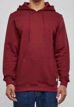 Sudadera color burdeos con un bolsillo delantero, capucha con cordón y mangas largas. Textura suave con puños y dobladillo acanalados, con una discreta etiqueta de logo.