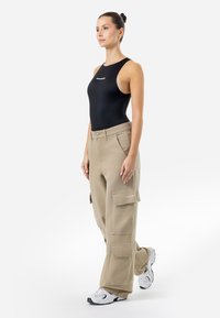 Svart ermeløs bodysuit, beige cargo-bukser med flere lommer, avslappet passform, bomullsblanding; kombinert med hvite treningssko.