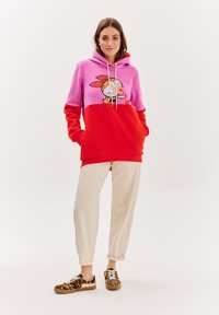 Mikina s růžovou horní částí a červenou spodní částí, zdobena kreslenou postavičkou. Kombinována se krémovými kalhotami a teniskami s leopardím potiskem.