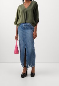 Olivgrünes V-Ausschnitt-Bluse mit Dreiviertelärmeln, kombiniert mit einem hochgeschnittenen blauen Jeansrock mit einem vorderen Schlitz und fransigem Saum.