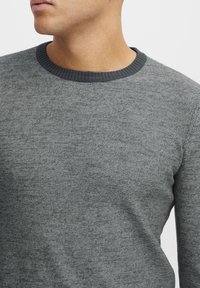 Gray sweater with a textured finish, crew neckline, and contrasting darker neckline trim. Material appears soft and knit.