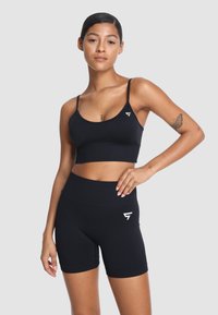 Czarny sportowy top z cienkimi ramiączkami i małym logo, w połączeniu z czarnymi szortami o wysokim stanie. Gładki, elastyczny materiał.