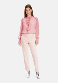 Rosa Bluse mit Pünktchen und Kragenband, durchsichtigen langen Ärmeln und taillierten Manschetten; kombiniert mit hellrosa maßgeschneiderten Hosen und silbernen Ankle Boots.