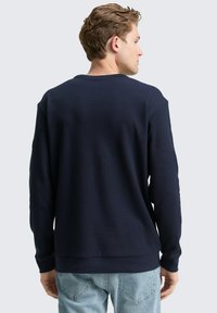 Marineblauwe waffle-knit sweatshirt met lange mouwen, ronde halslijn en geribde manchetten, gecombineerd met lichtblauwe jeans.
