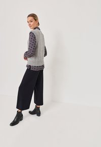 Suéter de punto gris sobre una camisa estampada con un fondo oscuro. Unos pantalones amplios negros y botas de tobillo completan el conjunto.