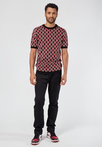 Camiseta de punto de manga corta con un patrón geométrico en rojo, negro y blanco, combinada con pantalones negros y zapatillas con acentos rojos.