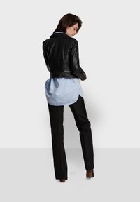 Black leather motorcycle jacket with a fitted design, zippered pockets, worn over a light blue shirt and black trousers.
