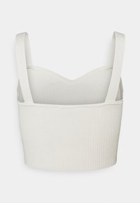 Bralette côtelé beige clair avec de larges bretelles et une coupe courte. Texture lisse et décolleté arrondi.