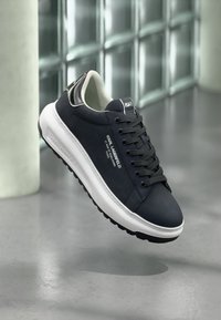 Navy blue sneaker with a smooth texture, white sole, black rubber outsole, and silver accents. Features logo detailing on the side.