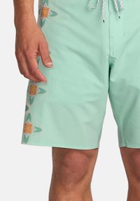 Costumi da bagno verde menta con un design laterale caratterizzato da vivaci motivi floreali, chiusura con cordino e tessuto liscio e testurizzato.
