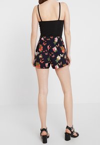 Czarna koszulka na ramiączkach w połączeniu z szortami w kwiatowy wzór w kolorze granatowym. Szorty mają elastyczny pasek w talii, długość do kolan oraz wyraziste wzory kwiatów i motyli.