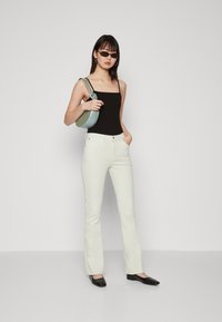 Jean flare blanc avec poches avant et texture subtile, associé à un débardeur noir ajusté et des ballerines à bout carré noires. Le sac à main est bleu clair.