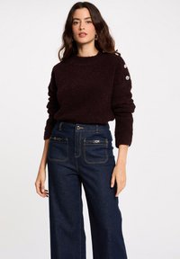 Maglione borgogna a trama con maniche lunghe e bottoni decorativi sulla spalla, abbinato a jeans a vita alta, larghi e blu scuro.