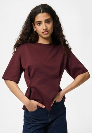 T-shirt bordeaux à manches courtes avec un col rond et une coupe décontractée, fabriqué en tissu en coton doux. Associé à un jean en denim bleu foncé.