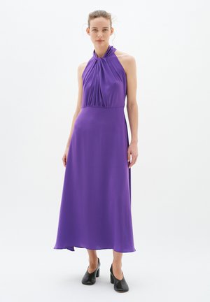 Robe mauve à encolure halter avec un corsage plissé, longueur maxi fluide et texture lisse. Associée à des chaussures à talons noirs.
