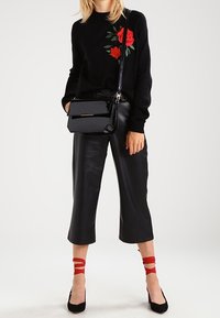 Czarny sweter z różowym haftem, zestawiony z krótkimi czarnymi spodniami. Eko-skórzana czarna torebka oraz czerwone skarpetki z paskiem do czarnych obcasów.