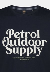 Námořnická modrá bavlněná tričko s bílým tučným textem "Petrol Outdoor Supply" a zelenou adresou pod ním. Kulatý výstřih, krátké rukávy.