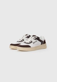 Hvite og brune sneakers laget av semsket skinn og syntetiske materialer, med rund tå, flate lisser og en strukturert beige yttersåle.
