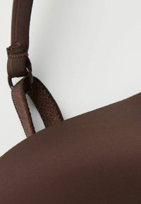 Bruine stoffen bh met een gladde textuur, voorzien van verstelbare bandjes, een platte naad en een metalen ringverbinding. Eenvoudig, minimalistisch ontwerp.