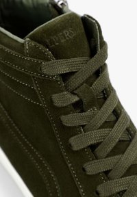 Zapatilla alta de gamuza verde con material texturizado, cordones planos y suela blanca en contraste. Los detalles incluyen costuras tonales y logotipo.