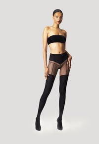 Collant neri trasparenti con dettagli opachi solidi, texture liscia e vita alta, abbinati a un top bandeau nero e tacchi alti.