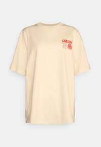 Beige bomulds t-shirt med rund hals og korte ærmer. Har et rødt grafisk print på den øverste venstre brystlomme, der siger "CHASING THE SUN."