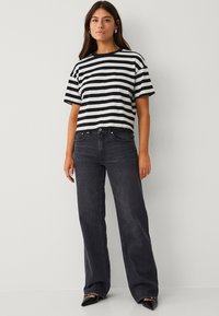 T-shirt rayé noir et blanc avec une coupe décontractée, manches courtes, associé à un jean en denim foncé taille haute et des chaussures noires pointues.