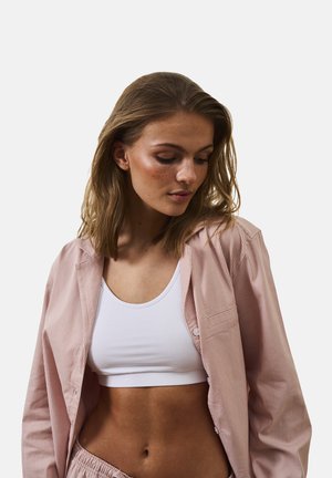 Camisa de botón a rayas rosa llevada sobre una camiseta sin mangas blanca, exhibiendo una textura suave y un ajuste relajado, con un detalle de bolsillo en la camisa.