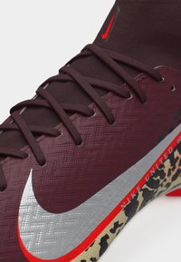 Κοντινό πλάνο μπορντό παπουτσιού ποδοσφαίρου Nike με σκούρα κορδόνια, ασημί λογότυπο, και σόλα με μοτίβο λεοπάρδαλης και κόκκινο κείμενο «NIKE UNITED».