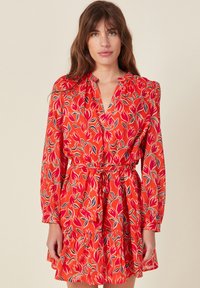 Punane lilleline kleit pikkade varrukatega, gathered vöökoht ja kihiline flounce seelik; omaduseks on violetsete ja roheliste lehe mustrid elava tausta ees.