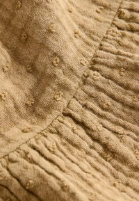 Textile in light beige with textured surface. Features raised dots and gathered sections creating rippled effect. Soft, natural fabric.