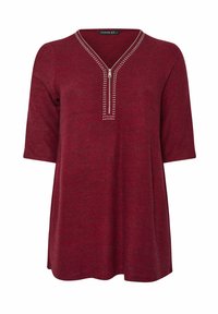 Top lungo bordeaux con maniche lunghe, scollatura a V e zip, impreziosito da borchie argentate lungo il collo. Tessuto morbido e testurizzato.