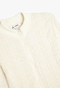 Cremfarbener Reißverschluss-Pullover mit einem Zopfmuster, geripptem Kragen und Bündchen sowie einer glatten Textur. Markenetikett sichtbar im Inneren.
