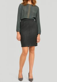 Tmavě šedá upnutá sukně spárovaná s texturovanou zelenou blůzou s vertikálním dekorativním pruhem. Outfit je doplněn šedými podpatky.