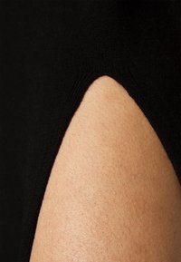 Tissu noir avec une découpe incurvée révélant une peau lisse marron clair en dessous, mettant en valeur le détail du vêtement et le contraste des textures.