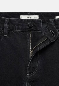 Jeans de mezclilla negra con cremallera, cierre de botón y costuras en blanco contrastantes. Etiqueta visible dentro de la cinturilla.