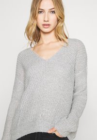 Hellgrauer Strickpullover mit V-Ausschnitt, langen Ärmeln und einem strukturierten Muster. Lockere Passform mit geripptem Saum und Bündchen.