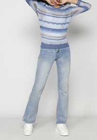 Pull en tricot bleu clair avec des rayures horizontales et un ourlet côtelé, associé à un jean évasé bleu clair et des baskets blanches.