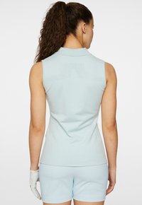 Ljusblå ärmlös polo med krage. Har textil med struktur och perforerade detaljer på baksidan samt en slät yta.