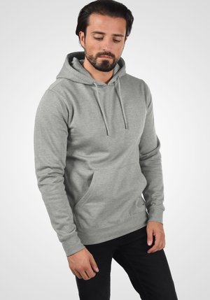 Sudadera gris con bolsillo tipo canguro, capucha ajustable con cordón y puños acanalados. La tela parece suave con una textura lisa sobre un fondo plain.