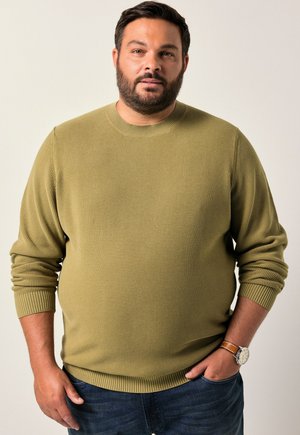 Maglione a coste verde oliva con scollatura rotonda e maniche lunghe. Indossato con jeans di denim, che mostrano un tessuto texturizzato.