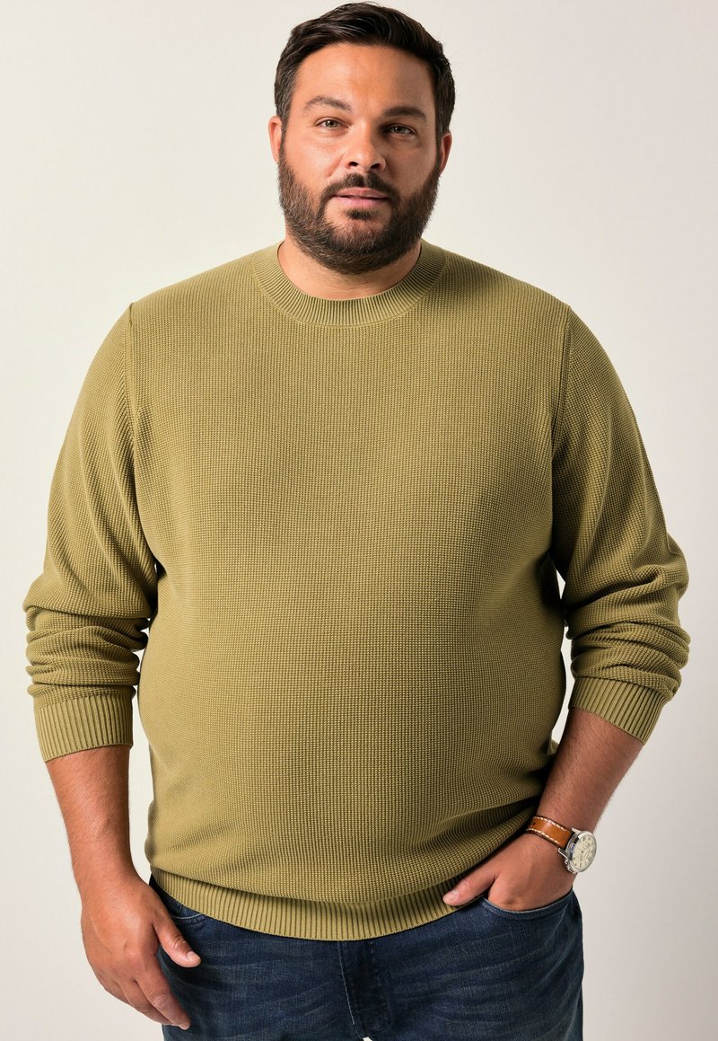 Maglione a coste verde oliva con scollatura rotonda e maniche lunghe. Indossato con jeans di denim, che mostrano un tessuto texturizzato.