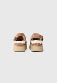 Sandali in suede beige con rivestimento in pelliccia sintetica, fascetta regolabile con fibbia e suola piatta di colore crema. Design semplice e funzionale.