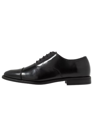 Chaussure Oxford en cuir noir poli, avec laçage fermé, bout droit et talon bas empilé, vue de côté sur fond blanc.