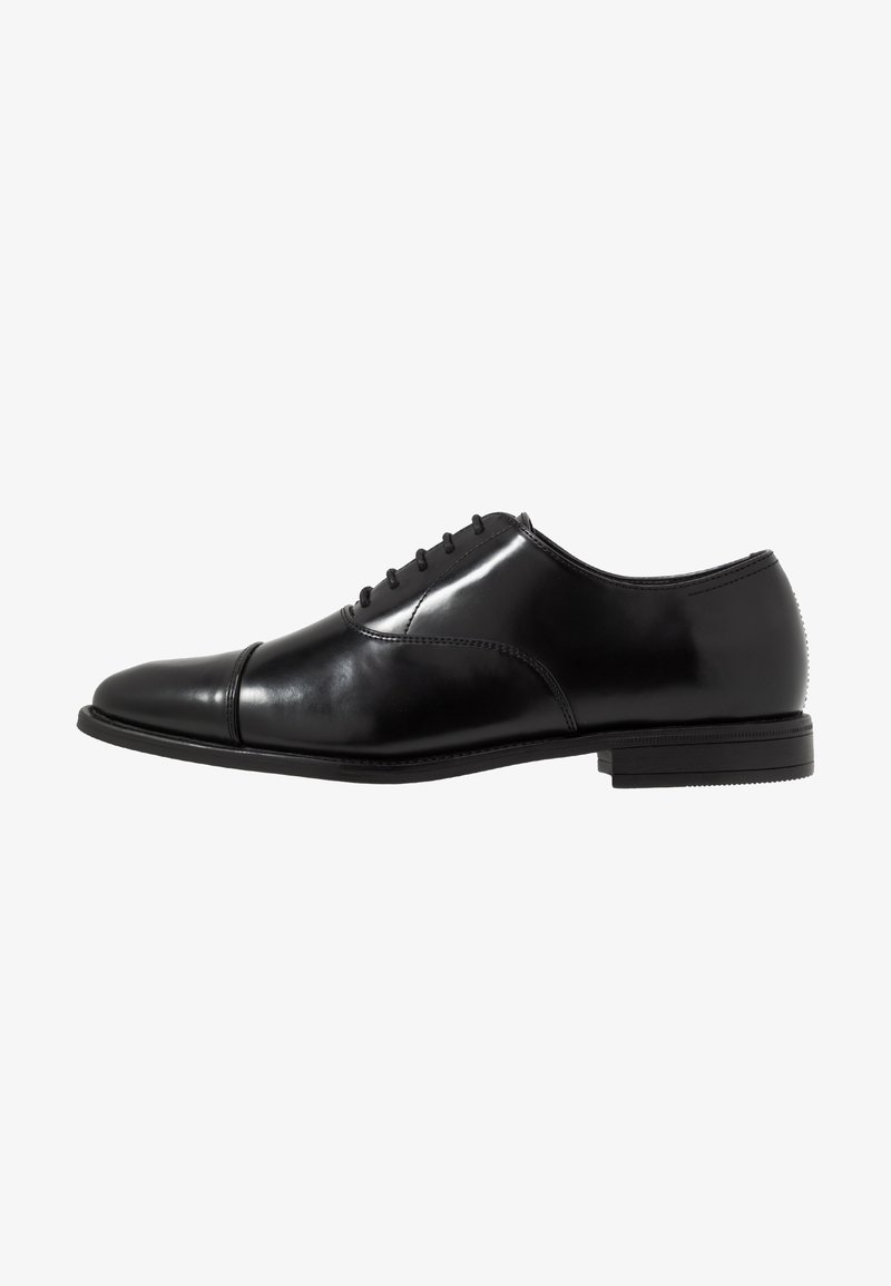 Chaussure Oxford en cuir noir poli, avec laçage fermé, bout droit et talon bas empilé, vue de côté sur fond blanc.