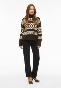 Rjava pletena majica z belimi geometrijskimi vzorci, rebrastimi manšetami in visokim ovratnikom, kombinirana s črnimi hlačami z ravnimi nogavicami in rjavimi čevlji s peto.