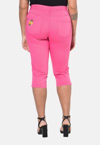 Vaaleanpunaiset caprihousut, joissa on istuva malli ja polveen asti ulottuva pituus. Housuissa on takataskut ja sitruunan kirjontayksityiskohta.