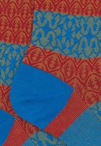 Colorful patterned fabric featuring intricate red, blue, and green designs. Notable texture with contrasting blue sections.