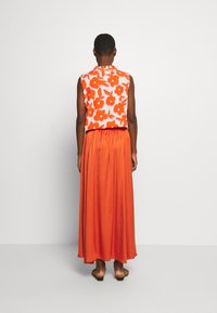 Florales, ärmelloses Crop-Top in Weiß mit orangefarbenen Blumen, kombiniert mit einem langen, fließenden orangefarbenen Rock. Glatter Stoff und elastischer Bund.